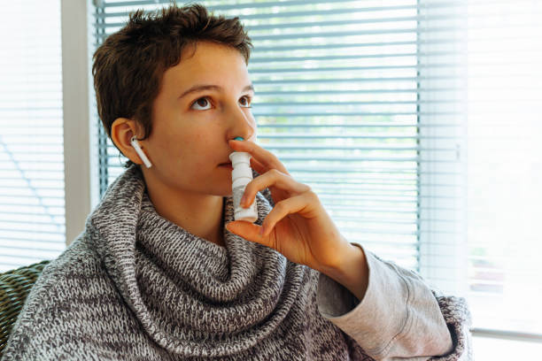 Colds or allergic seasonal diseases in cold weather, Young teenage girl with short haircut treats cold or allergic rhinitis with medicinal nasal spray, sitting in warm sweater at home, close-up sneezeweed stock pictures, royalty-free photos & images