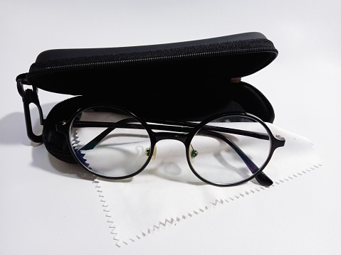 Round glasses with black case on top of white cleaning cloth