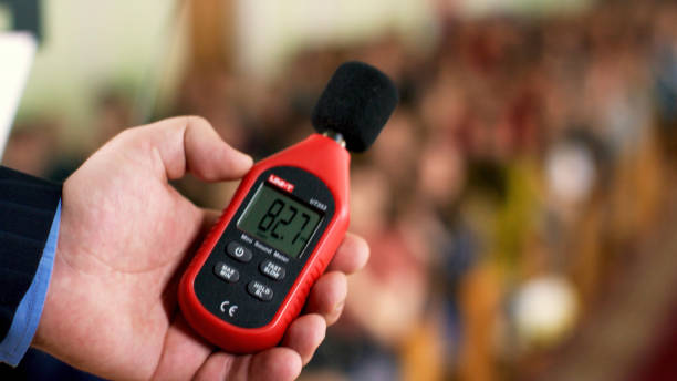 Close up of a man hand holding a red sound level meter and analyzer on clapping audience background. Stock footage. Man measuring the noise level on blurred crowd background. Close up of a man hand holding a red sound level meter and analyzer on clapping audience background. Man measuring the noise level on blurred crowd background. industrial music stock pictures, royalty-free photos & images