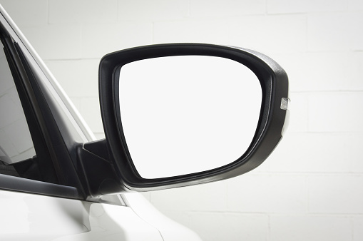 Close up of side mirror on a modern white car with white brick wall in the background. Selective focus on mirror with cut out.