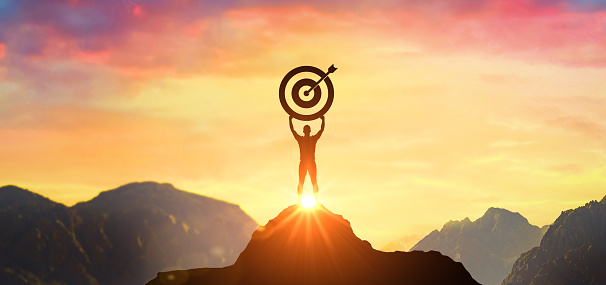 Successfully achieving your goal. Success Business Leadership, Winner on top. Silhouette businessman holding target on top mountain, sky and sun light background. Business success and goal concept