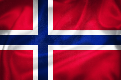 Norwegian flag in red white and blue waving in the breeze agains the blue sky.
