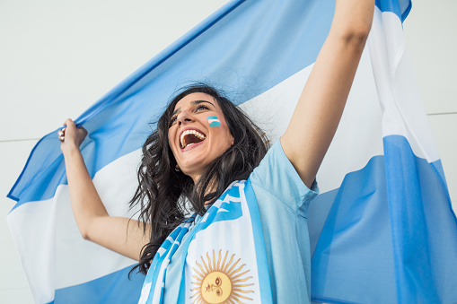 Young woman soccer fan cheering at the game. Holding national team flags, with color paint on face. Studio shot