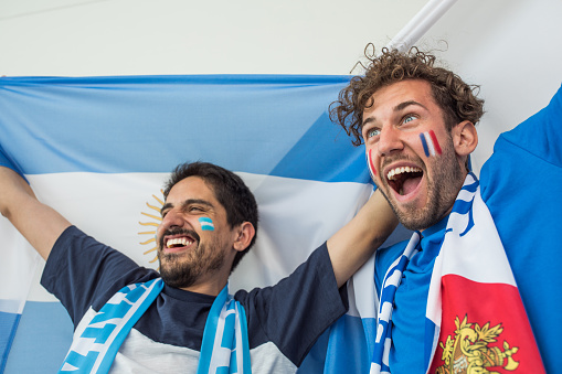 Group of young multi-ethnic soccer fans cheering at the game. Holding national team flags, with color paint on faces. Studio shot