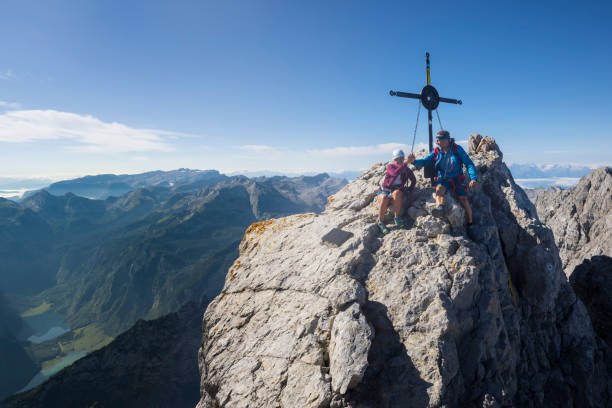 zwei bergsteiger auf dem gipfelkreuz auf dem watzmann-bestand - watzmann stock-fotos und bilder