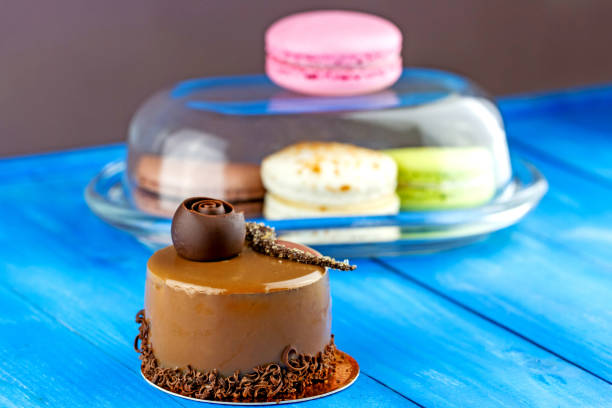 Caramel cake decorated chocolate shavings with colorful macaroons behind on blue wooden background
