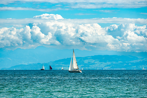 Cruising sailboats on German north side of Lake Constance in clear weather. Panorama with Swiss and Austrian Alps in background.