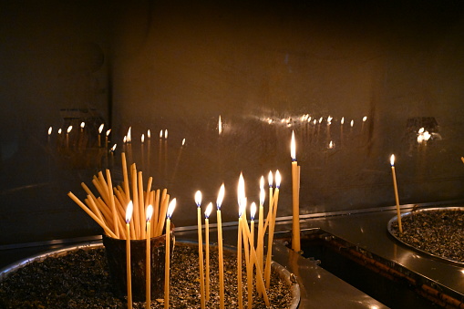 Thin long candles burning in a church.  Close up view. The flames are reflecting on the glass wall on the background. There is copy space available as well.