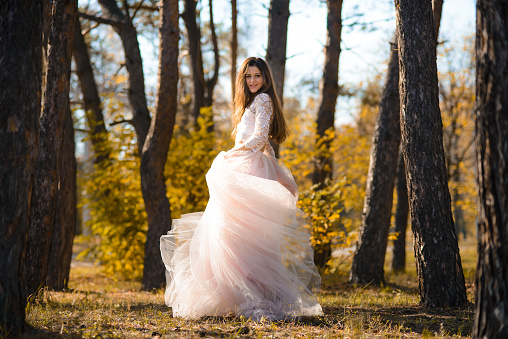 girl in magnificent beautiful wedding dress is spinning in pine forest in sun