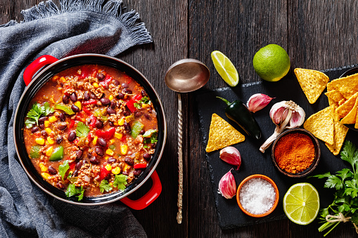 taco soup of ground beef, tomatoes, chopped green chilis, onions, corn, red beans and taco seasoning in red pot with ingredients on stone board, high angle view, flat lay, close-up