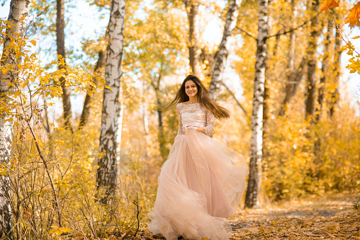 A girl in a long light pink puffy dress runs through the autumn birch forest