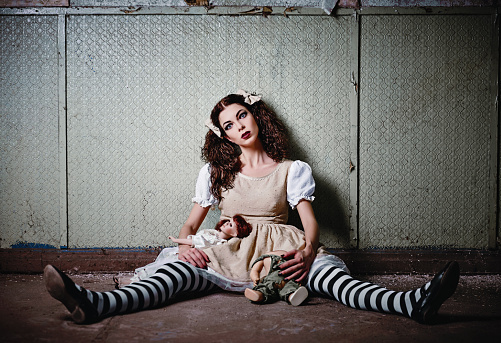 Weird girl with dolls sitting in abandoned place