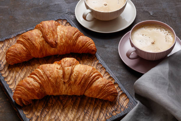 istock Fresh croissant with two cup of coffee on dark brown background. 1427146258