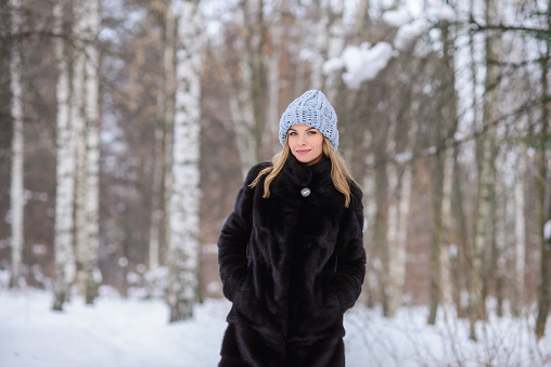 portrait of a beautiful fair-haired girl in a blue hat, black fur coat against the backdrop of a snowy winter birch forest