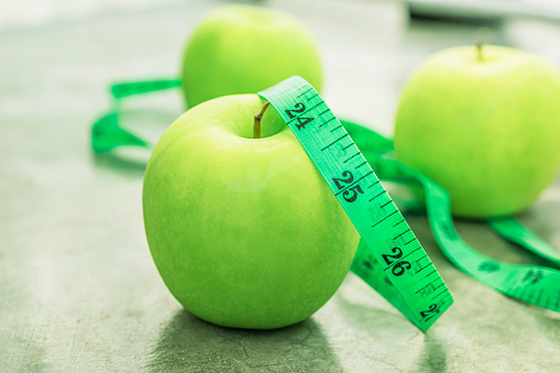 Measure tape and green apple on stone background close up, healthy food concept.