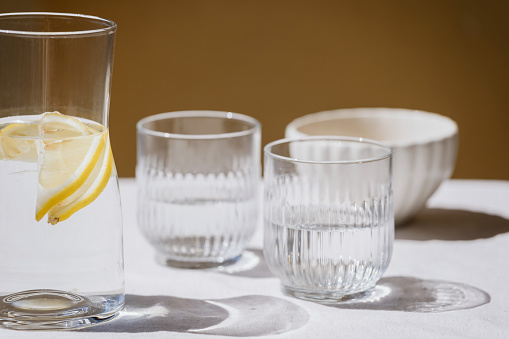 closeup of table serving with linen tablecloth, ceramic bowl, two glass cups and pitcher with fresh lemon drink at home kitchen