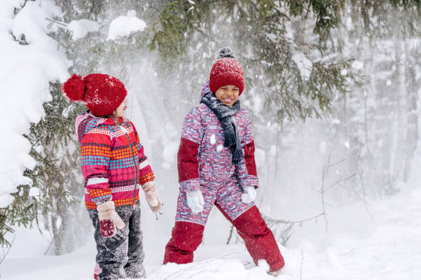 Happy Caucasian and African-American girls are walking in a winter park, shaking snow from snow-covered trees.Winter fun,active lifestyle concept