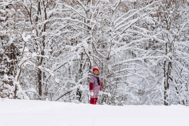 Happy little African-American girl in a red hat and jumpsuit walks in the winter forest.Beautiful trees are covered with white snow.Winter fun,active lifestyle concept.