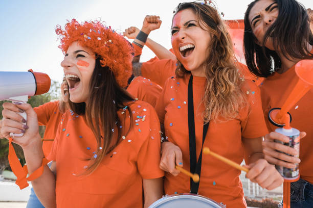 оранжевые спортивные болельщики кричат, поддерживая свою команду вне стадиона - сосредоточьтесь на лице левой девушки - dutch culture soccer fan orange стоковые фото и изображения