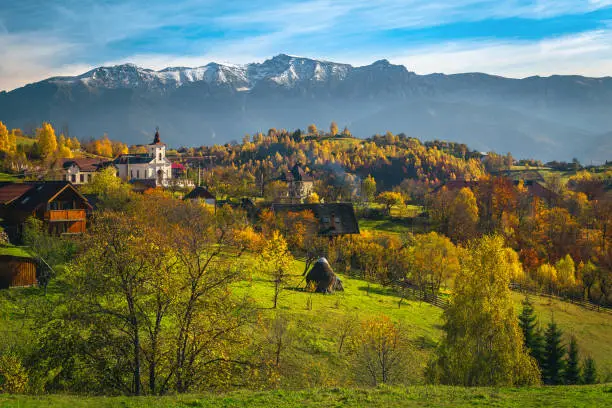 Stunning autumn rural landscape and colorful deciduous trees on the hills. Colorful autumn forest on the slope and snowy mountains in background, Carpathians, Transylvania, Romania, Europe