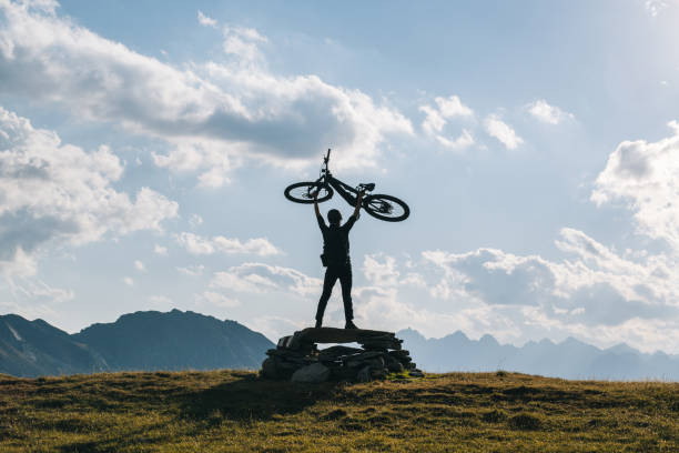 un homme tient un vélo de montagne électrique au-dessus de sa tête, dans une prairie alpine - success determination idyllic carefree photos et images de collection