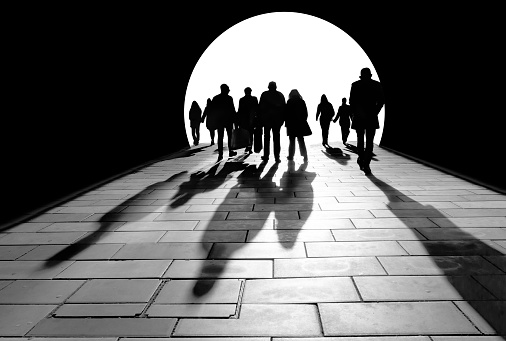 silhouettes of crowd of people walking towards the light, casting long shadows on he floor