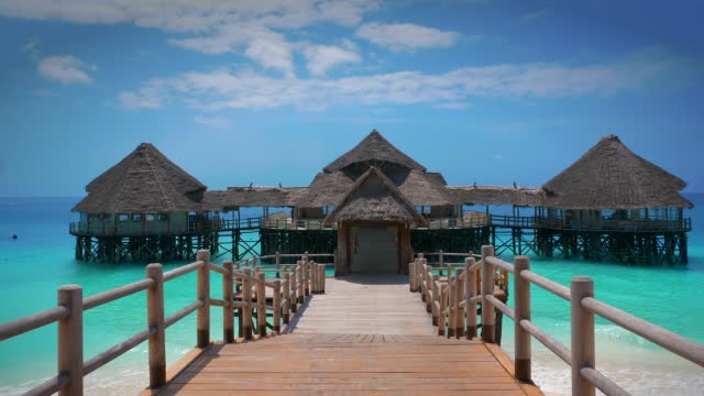 Stilt hut with palm thatch roof washed with turquoise Indian ocean waves on the white sand sandbank beach on Zanzibar island, Tanzania