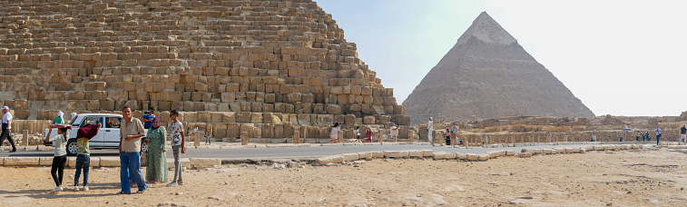 Giza, Cairo, Egypt - September 30, 2021: Panoramic view of the pyramids of Giza, a complex of ancient monuments on the Giza plateau. People walk and take pictures near the pyramids.