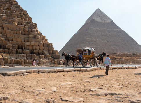 Pyramids of Giza, Giza Necropolis, Egypt - March 12, 2023: Egyptian man riding a camel at the Pyramids of Giza.\n\nThe Giza Necropolis is a large area near Giza, a suburb of Cairo that has many tombs and burial sites. It is also where you can find the famous Pyramids of Giza, the Great Sphinx, and more. The name comes from the ancient Greek word nekropolis, which literally means “city of the dead”.\n\nThe Giza Complex was once near the ancient Egyptian capital of Memphis, and the Giza plateau is where a number of pharaohs, queens, and nobles of the Fourth Dynasty of ancient Egypt were buried. \n\nAll three of Giza's pyramids and their elaborate burial complexes were built  from roughly 2550 to 2490 B.C. The pyramids were built by Pharaohs Khufu, Khafre, and Menkaure.