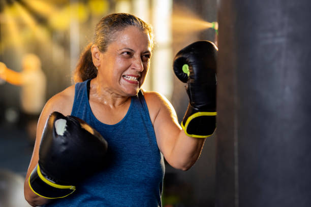 Female boxer training with punching bag Aggressive old woman in sportswear training with boxing bag in gym women boxing sport exercising stock pictures, royalty-free photos & images