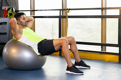 Young man stretching on exercise ball at gym