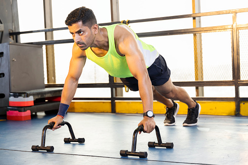 Active muscular man in sportswear doing push ups with bars at gym