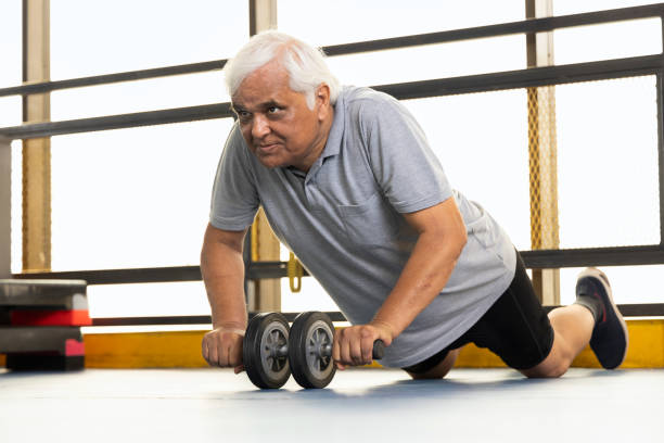 senior man strengthening her body by using the abdominal wheel Active old man in sportswear using abdominal exercise roller for stretching forward older people stock pictures, royalty-free photos & images