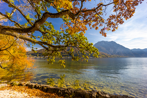 Lake with reflection of mountains at sunrise in autumn in Dolomites, Italy. Landscape with Antorno lake, blue fog over the water, trees with orange leaves and high rocks in fall. Colorful forest