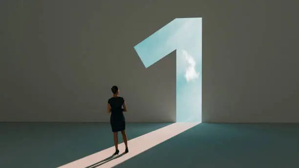 Woman stands in front of  a big number one symbol that lights up. She is surrounded by darkness, but walks on a path of sunshine reaching first place. Note: Digitally generated image.