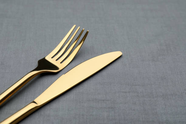 istock Golden fork and knife on grey table, closeup. Space for text 1427236230