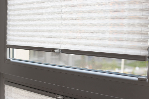 Pleated blinds close up on the window in the interior. Home blinds - cordless pleated modern shades on apartment windows. White color fabric. Bottom up top down pleated curtains.