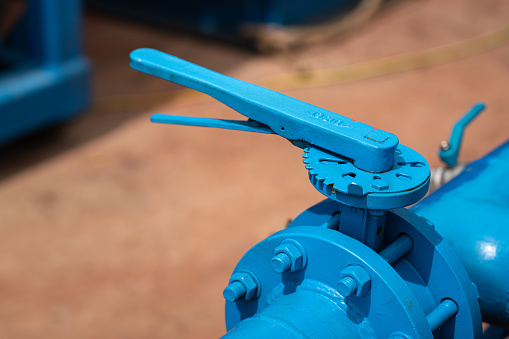 Handle controlling gate valve of water pumping unit which is used in oil field operation. Heavy industrial equipment object, close-up and selective focus at the valve handle.