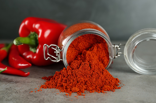 Glass jar of paprika with red peppers on light grey table, closeup