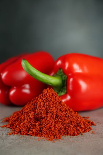 Heap of paprika with sweet bell peppers on light grey table, closeup