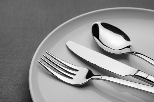 Plate with shiny silver cutlery on grey table, closeup