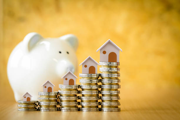 Home model put on the stack gold coin with growing interest and blurred piggy bank on the back put on the desk in the office, Saving money for buy house or loan for investment of real estate concept. modelo de casa puesto en la pila de moneda de oro con creciente interés y alcancía borrosa en la parte posterior puesta en el escritorio en la oficina, ahorro de dinero para comprar casa o préstamo para la inversión de concepto inmobiliario