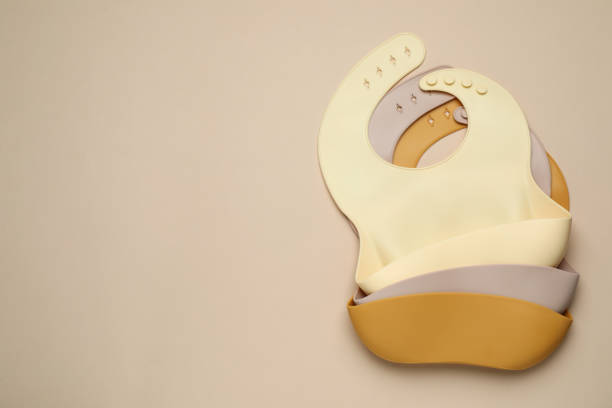 istock Three silicone baby bibs on beige background, top view. Space for text 1427247102