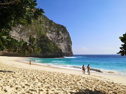Tourists relaxing on the amazing Kelingking beach on the coast of Nusa Penida island, Bali, Indonesia