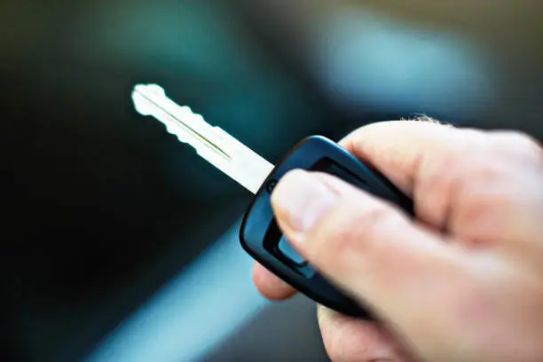 Man's hand holding a car key beside a vehicle.