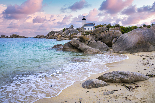 The Pontusval lighthouse, located on a rocky point in northern Finistere in Brittany, overlooks a sea of transparent turquoise waters during sunrise.