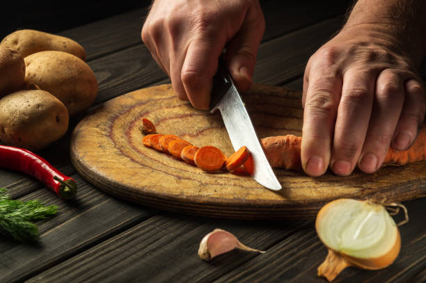 istock Slicing carrots on a wooden board for cooking. Chef hands with a knife while working on the kitchen table. Peasant foods. 1427253783