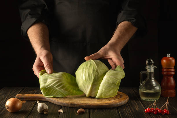 o chef ou cozinheiro faz uma salada de repolho fresco. preparação para cortar na cozinha. ideia de dieta vegetal ou culinária vegetariana - hotel commercial kitchen organic salad - fotografias e filmes do acervo