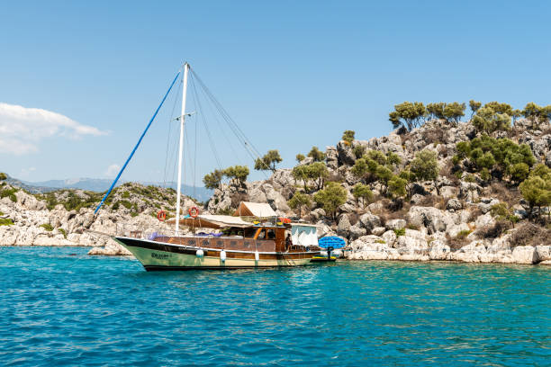 Mediterranean coastline in the Kekova region of Antalya province in Turkey Kalekoy, Antalya, Turkey - August 14, 2021. Mediterranean coastline in the Kekova region of Antalya province in Turkey, with a turing single-mast gulet boat. kekova stock pictures, royalty-free photos & images