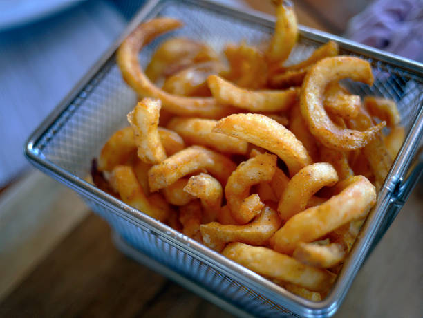 High angle view Close up of Curly fries (Fried Potato) breaded serving in the Mesh Bucket on Wooden table, blurry background, selective focus High angle view Close up of Curly fries (Fried Potato) breaded serving in the Mesh Bucket on Wooden table, blurry background, selective focus curly fries stock pictures, royalty-free photos & images